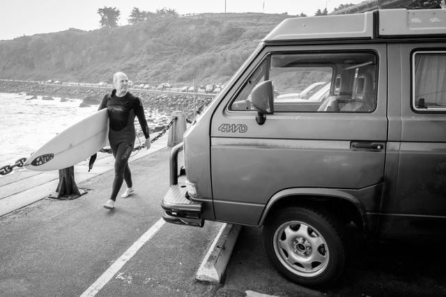 A surfer walking in front of a Volkswagen Bus at Fort Point, San Francisco.