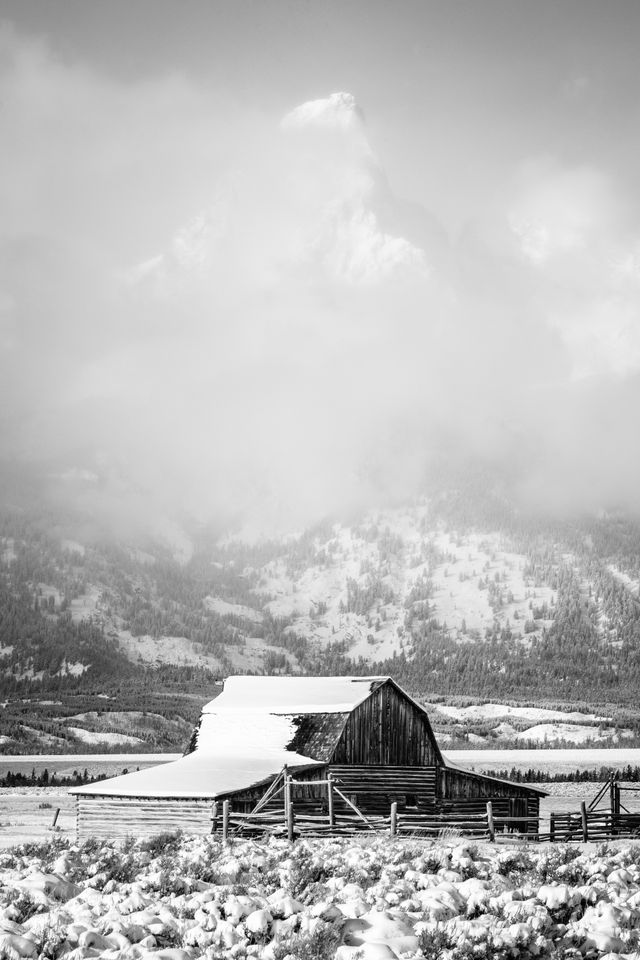 The John Moulton barn at Mormon Row, after a snowstorm. Grand Teton can be barely seen through the clouds in the background.