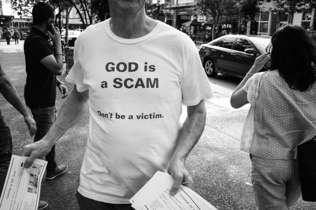 A man wearing a shirt that says "god is a scam, don't be a victim" while handing out pamphlets that read "campaign to kill Jesus".