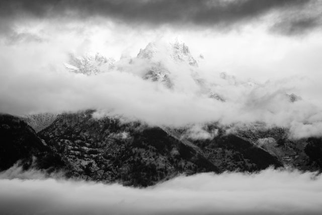 Teewinot Mountain, covered in snow after a storm, behind layers of clouds.