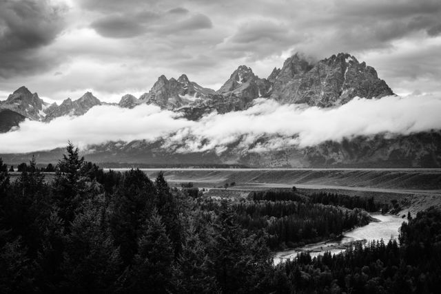 The Teton range on a stormy afternoon, from the Snake River Overlook. Grand Teton is hidden in the clouds, and a band of clouds is floating along the middle of the range.