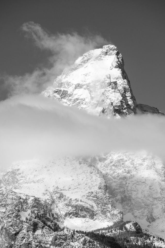 Grand Teton, covered in snow, and with a layer of clouds along the middle of the mountain.