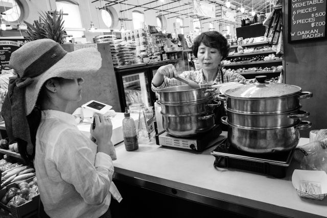 A customer shopping for dumplings at Eastern Market, while the salesperson pulls them out of the steamer and into the container.