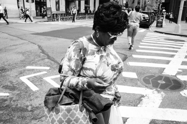 A woman wearing sunglasses crossing Broad Street in New York's Financial District.