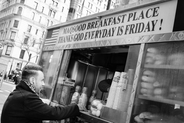 A man buying breakfast from a cart with a sign that says "thanks god everyday is friday!" [sic]