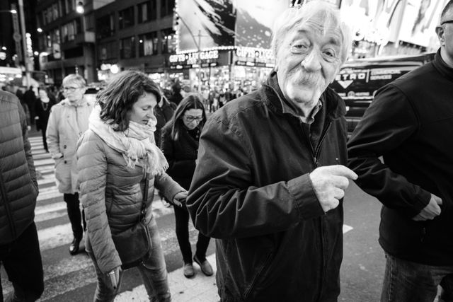 A person with a very bushy mustache smiling at the camera and crossing the street near Times Square.