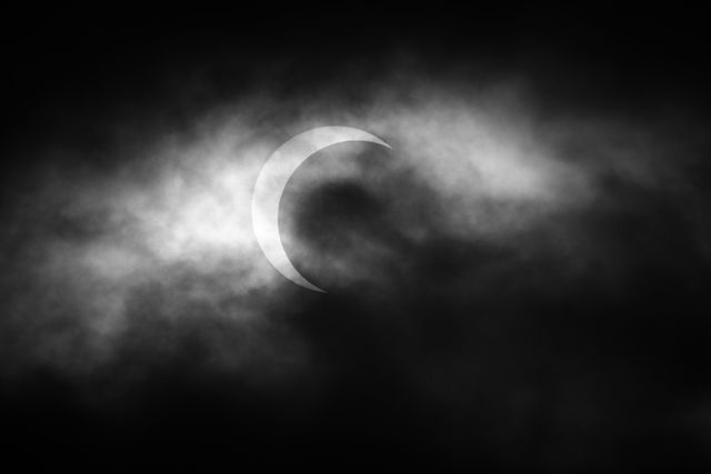 A partial annular solar eclipse seen through the clouds, with the Moon eclipsing the Sun about three quarters of the way.