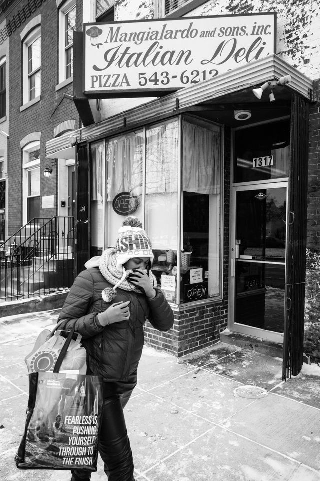 A woman protecting her face from the cold with her scarf, as she walks in front of a sandwich shop on Capitol Hill.