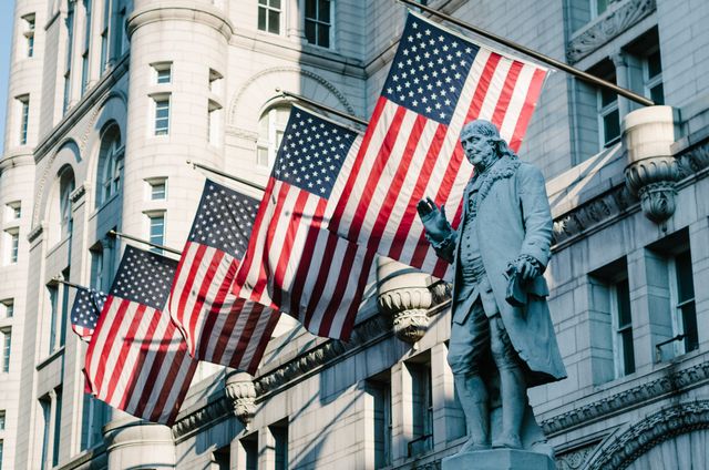 Statue of Benjamin Franklin at the Old Post Office building in Washington, DC, in front of several flags of the United States.