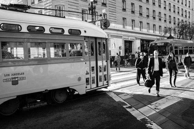 Pedestrians crossing the street in front of an old streetcar on Market Street.