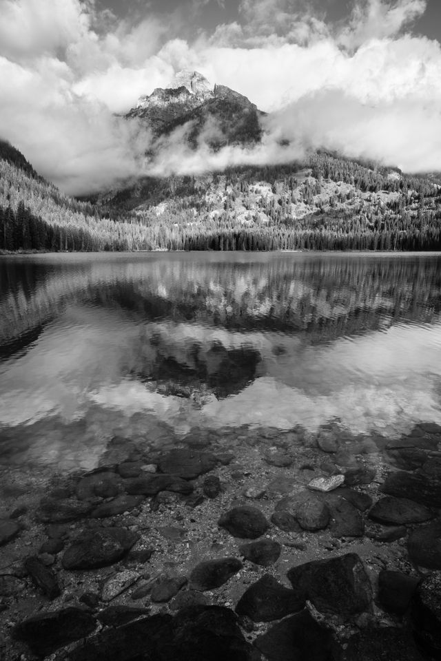 Nez Perce Peak reflected off the surface of Taggart Lake. In the foreground, rocks under the surface of the lake.