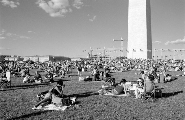 People sitting on the lawn in front of the Washington Monument.