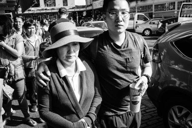 A young man walking with his arm around an older lady wearing a hat on Pike Place Market.