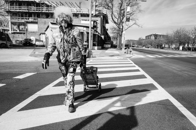 A smiling man wearing enormous crystal-studded headphones and sunglasses and a sweater with "Happy Stan" embroidered on it, crossing 12th Street SE in Capitol Hill.