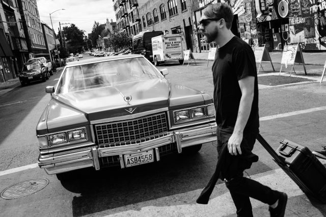 A man with a rolling suitcase crossing the street in front of a cool old Cadillac on Capitol Hill, Seattle.