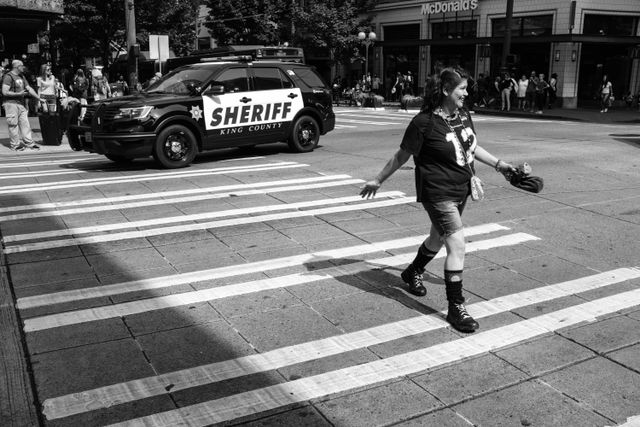 A woman smiling and crossing the street while a sheriff SUV drives past her, on Pine Street in Seattle.