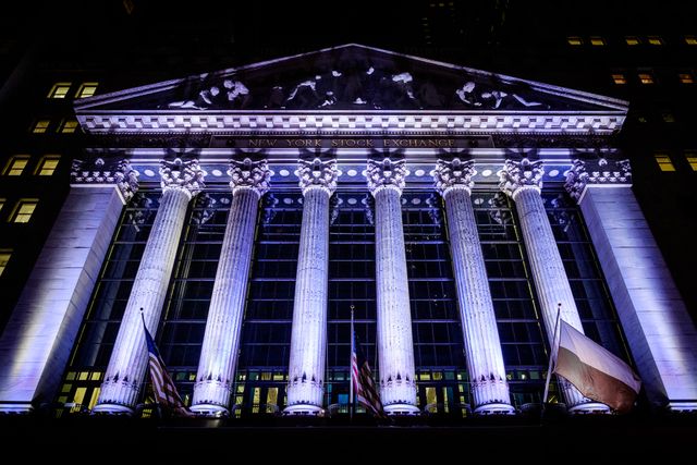 The New York Stock Exchange building, lit up in purple lights at night.