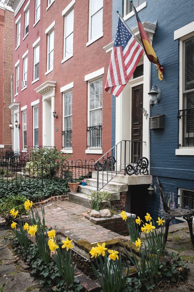 A row house in Capitol Hill, with yellow daffodils in bloom in the front yard, and American and German flags next to the front door.