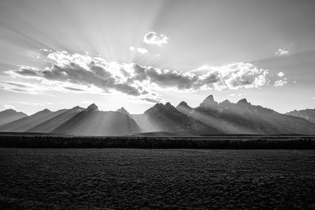 The sun setting behing some clouds, shedding sunbeams all over the Tetons.