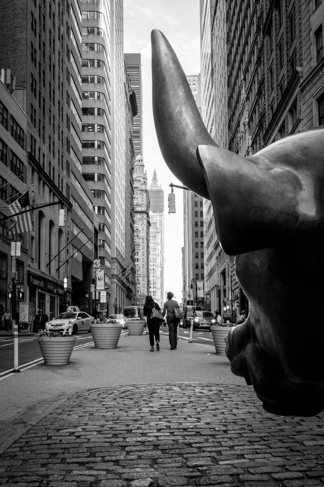 Two pedestrians walk on Broadway in front of the Charging Bull.