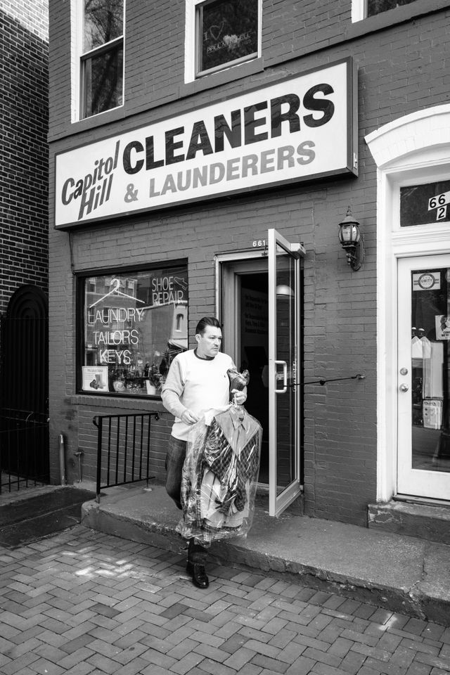 A man walking out of Capitol Hill Cleaners & Launderers with his dry cleaning on Eastern Market.