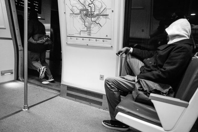 A man sitting on a Metro train while another guy runs out.