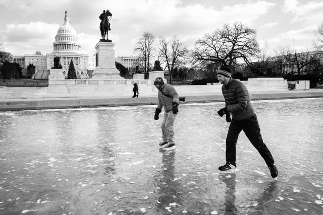 Two people ice skating on the frozen Capitol Reflecting Pool, in front of the Ulysses S. Grant Memorial and the United States Capitol.