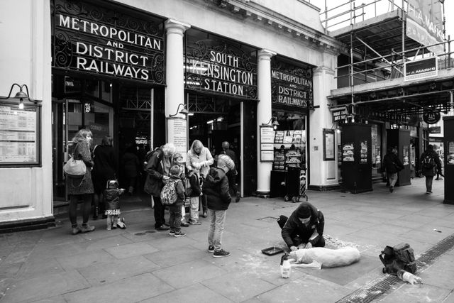 A man sculpting a dog out of sand in front of the South Kensington Station in London.