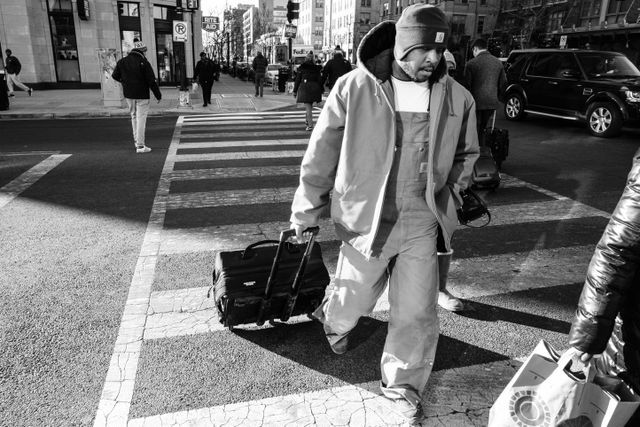 A man pulling a suitcase across the street near U Street NW.