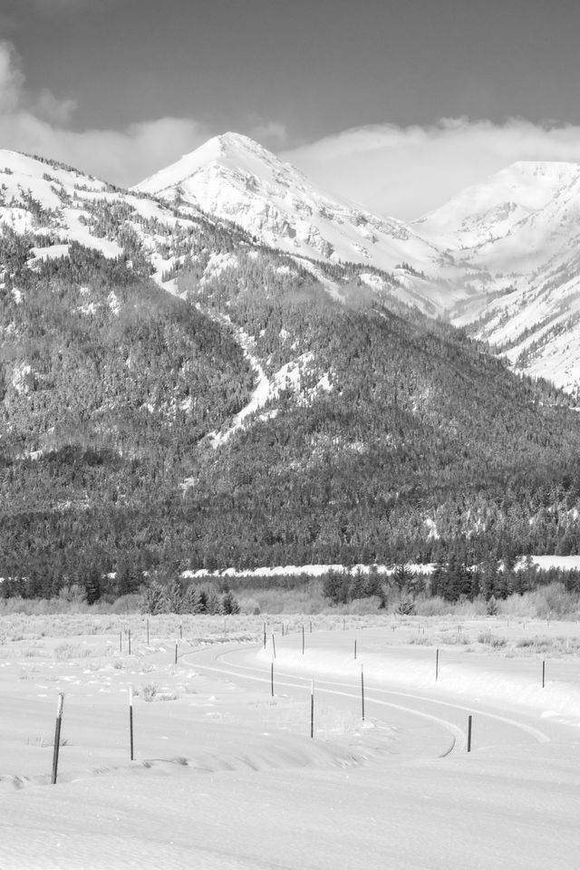 A winding road in the snow leading towards the Circle EW Ranch, with the Teton range in the background.