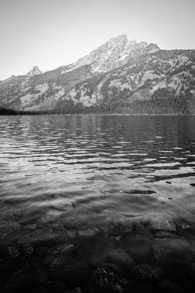 Teewinot Mountain seen from the shore of Jenny Lake. In the foreground, rocks under the surface of the lake.