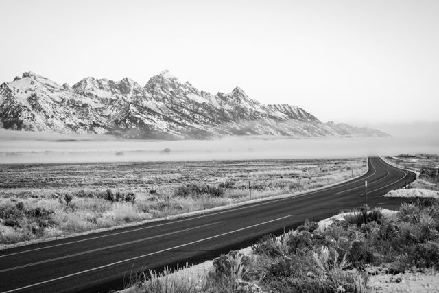 The Tetons, blanketed in fog at sunrise, with the main park road in the foreground.