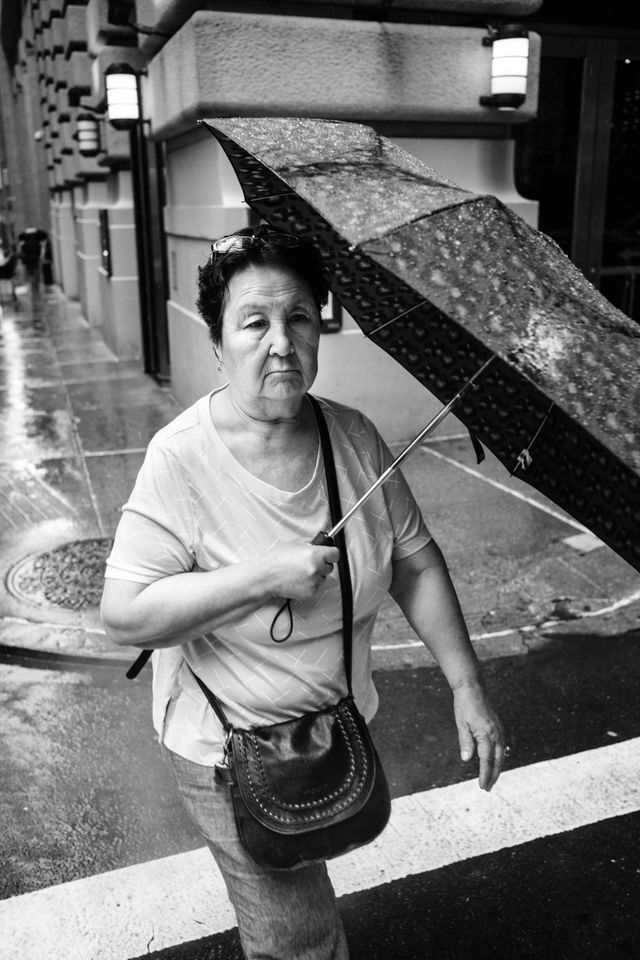 A woman carrying an umbrella in the rain, on the intersection of William & Pine streets in New York City.