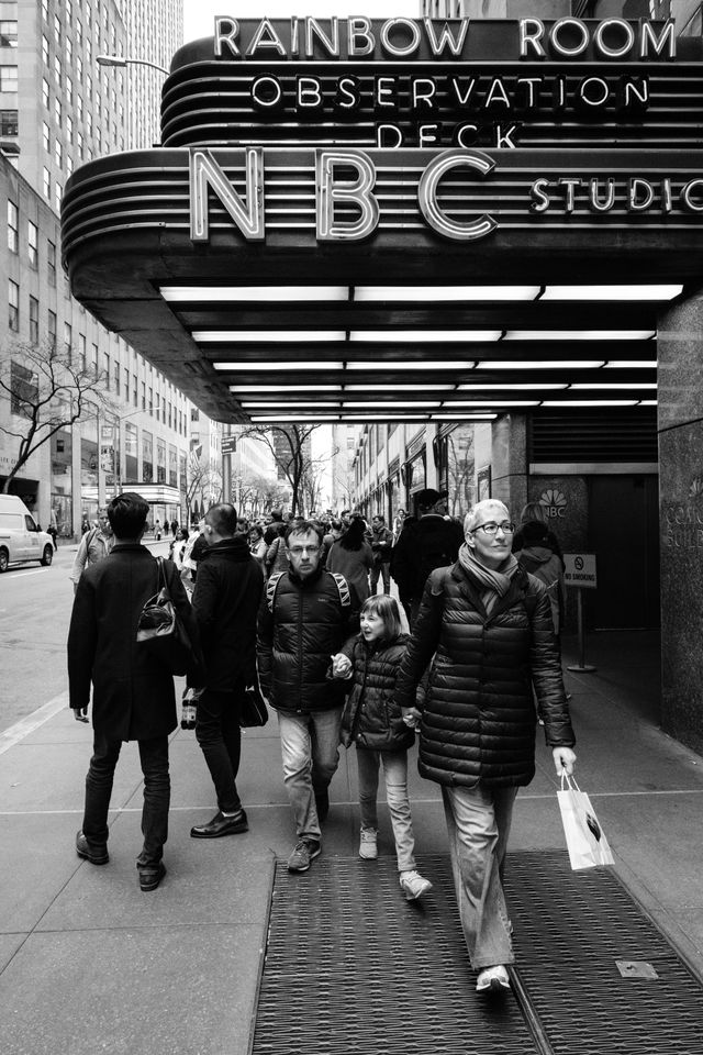 A family holding hands while walking by Rockefeller Center in New York City.