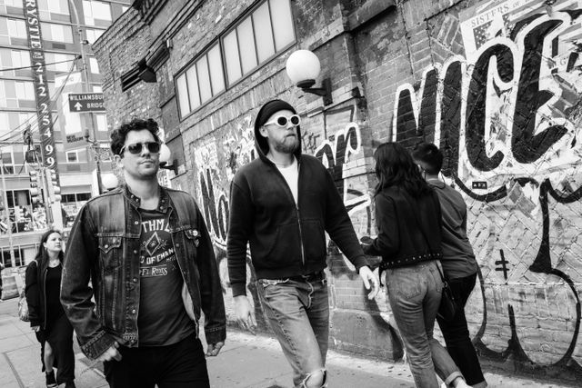 Two men wearing sunglasses and walking in front of a graffiti'd wall in Manhattan's Lower East Side.