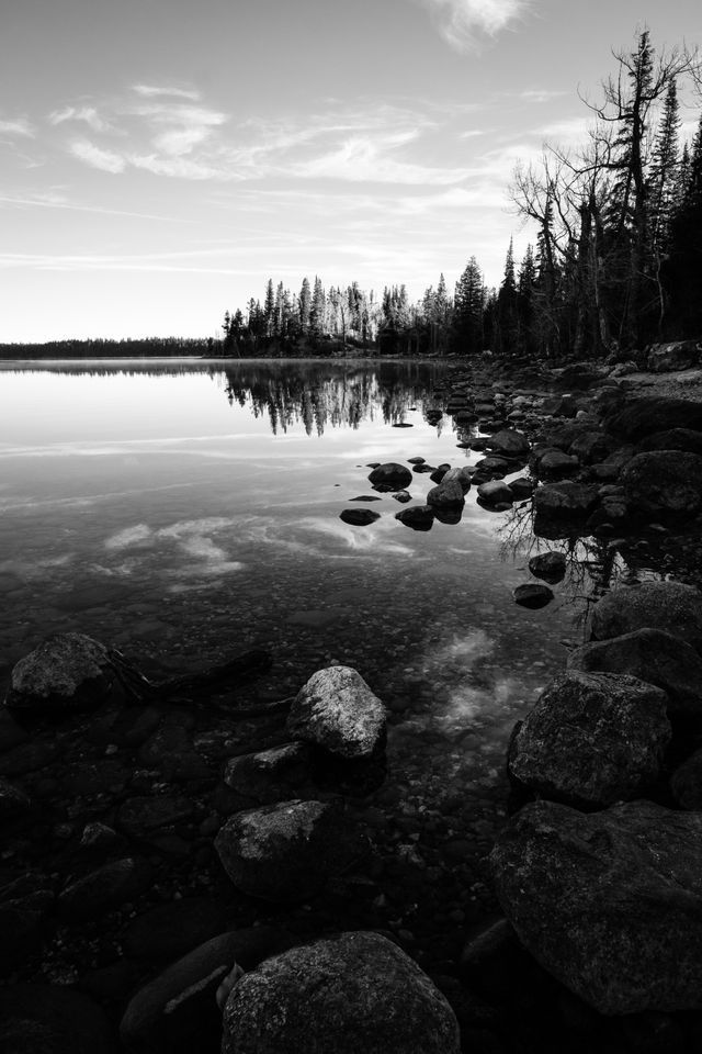 Rocks, trees, and clouds reflected off the waters of Jenny Lake at Grand Teton National Park.