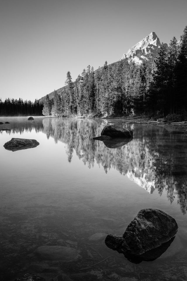 Three large boulders rising from the water at String Lake. In the background, Teewinot Mountain.