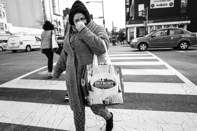 A woman scratching her nose while crossing the street at 14 and U.