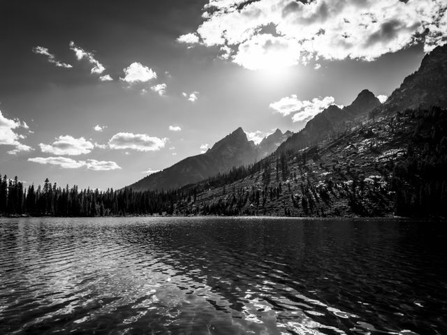 The Teton Range, including Teewinot Mountain, Grand Teton, and Mount Owen, seen backlight by the Sun, from the surface of String Lake.