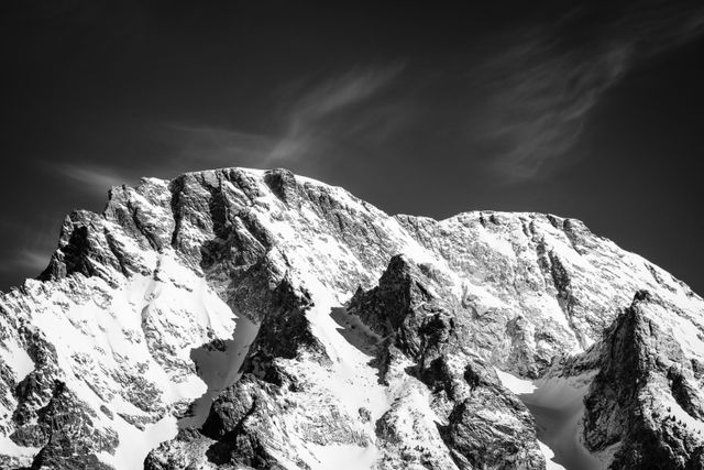 A close-up of the summit of Mount Moran, covered in snow, under wispy clouds.