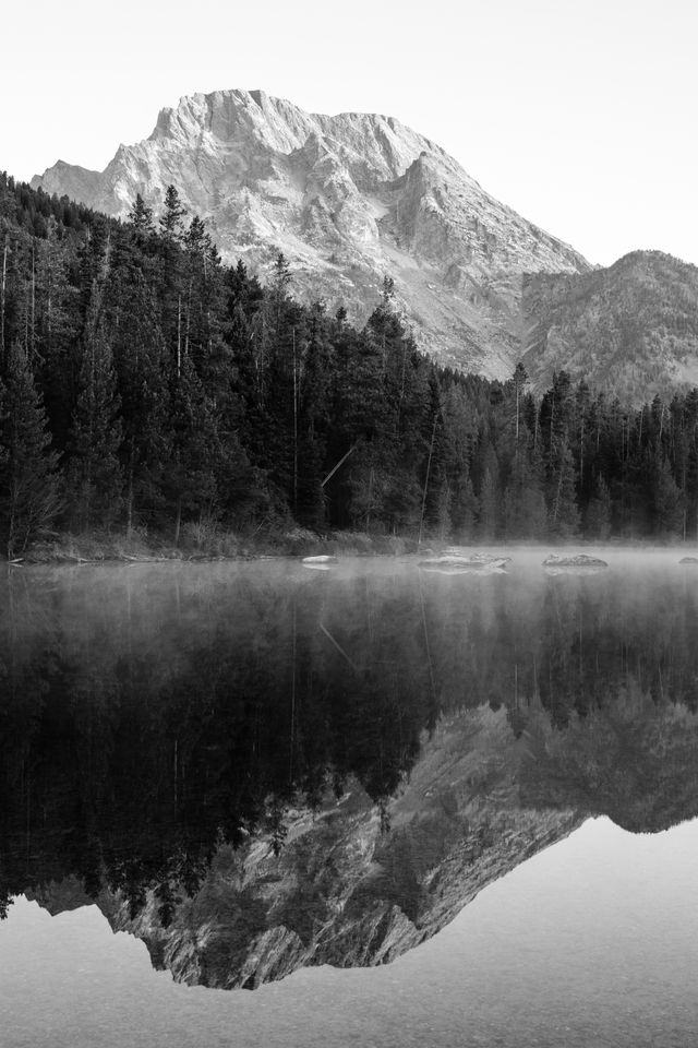 Mount Moran, reflected off the surface of String Lake at dawn. Rocks and mist can be seen on the surface of the lake.