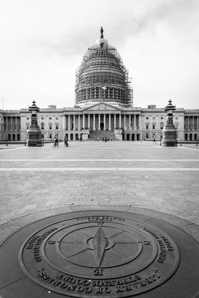 The compass on the grounds of the United States Capitol, with the scaffolding-covered dome in the background.