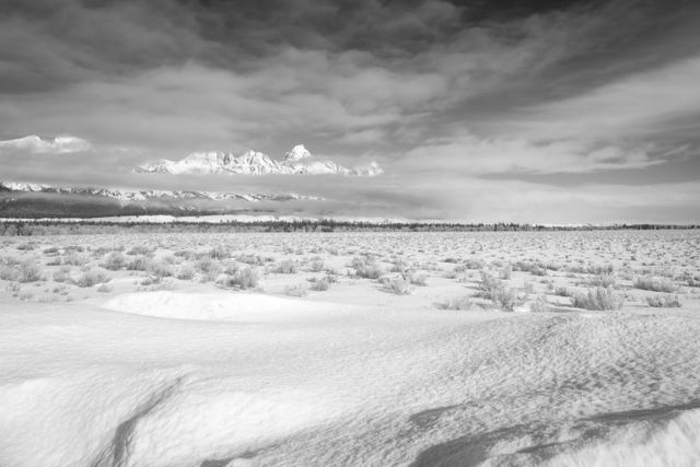 Grand Teton, seen behind the clouds in the background of a snow-covered field.