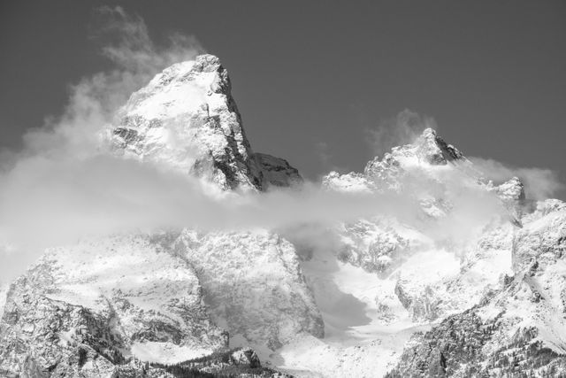 Grand Teton and Mount Owen. Both mountains have heavy snow cover, and a layer of clouds is in front of them.