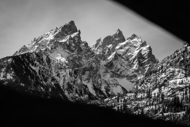 Teewinot Mountain, Grand Teton, and Mount Owen, covered in snow and framed by the beams of a wooden bridge.