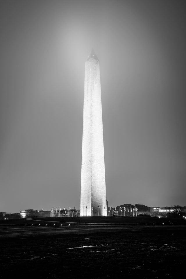 The Washington Monument, seen illuminated at night through fog on the National Mall.