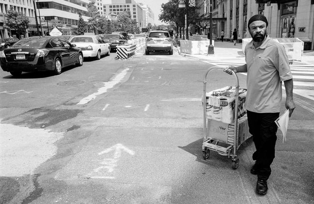 A person carrying a cart with rolls of paper towels and a box of Diet Cokes.