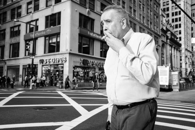 A man smoking a cigarette while crossing Broadway in New York's Financial District.