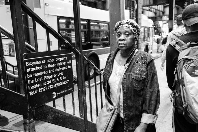 A woman in a denim jacket walking on Broadway, next to the stairs leading up to the Marcy Avenue subway station in Williamsburg.