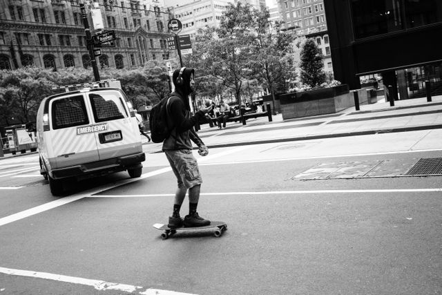 A man riding a skateboard while eating an apple, on Broadway, in the Financial District.